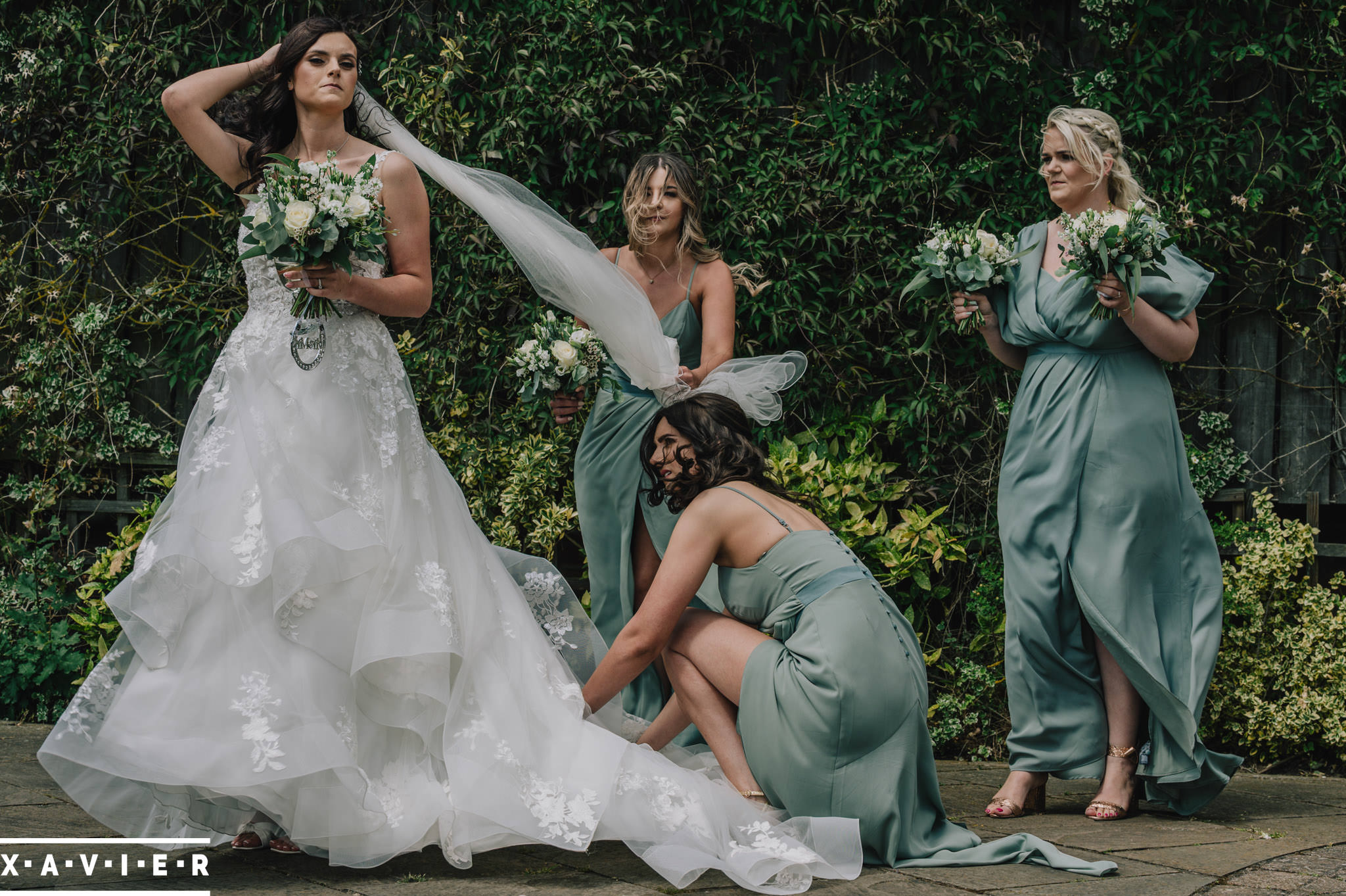 bridesmaids help the brides dress as it bl;ows in the wind