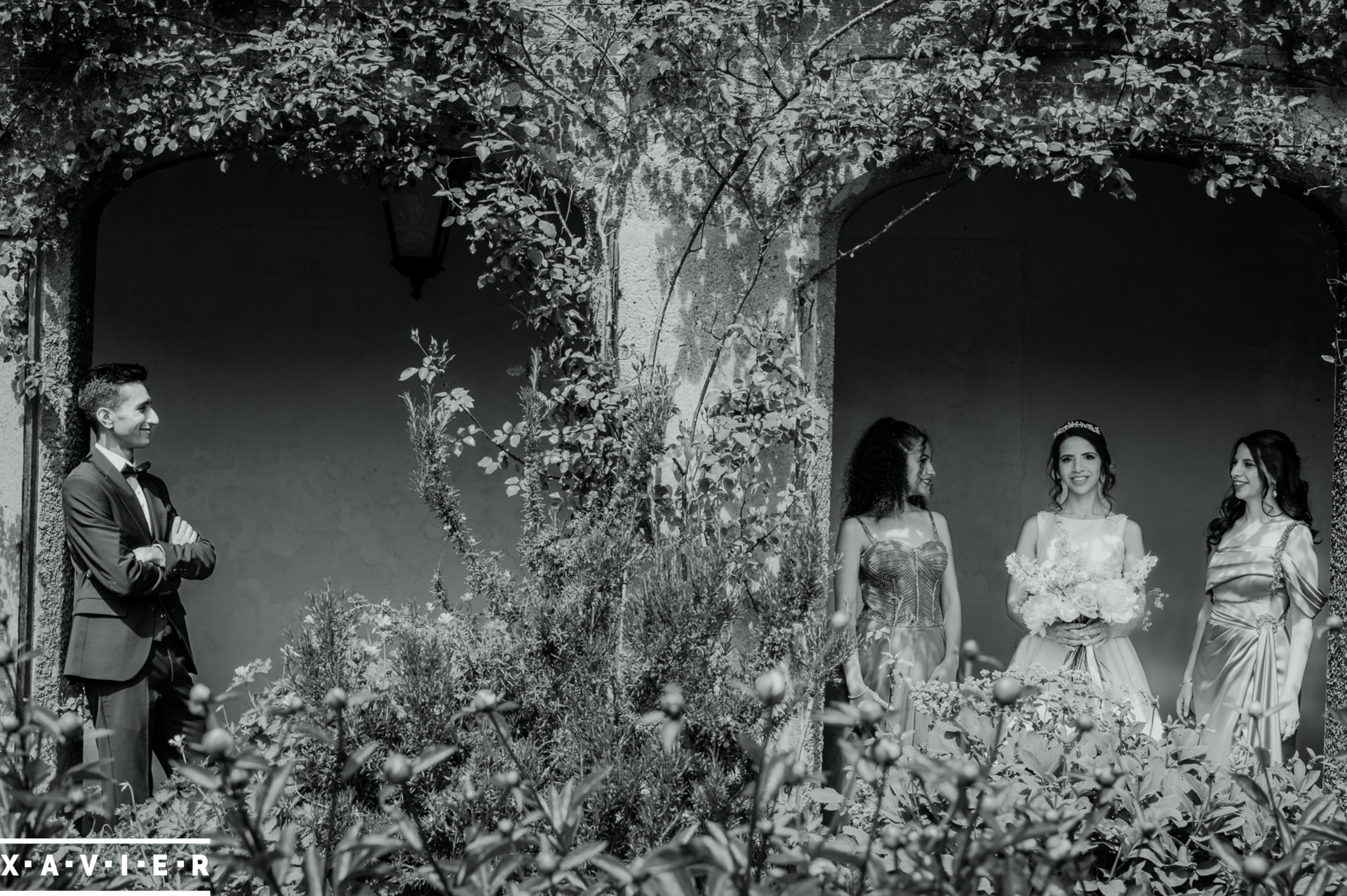 bride and groom stand with bridesmaids un the arches