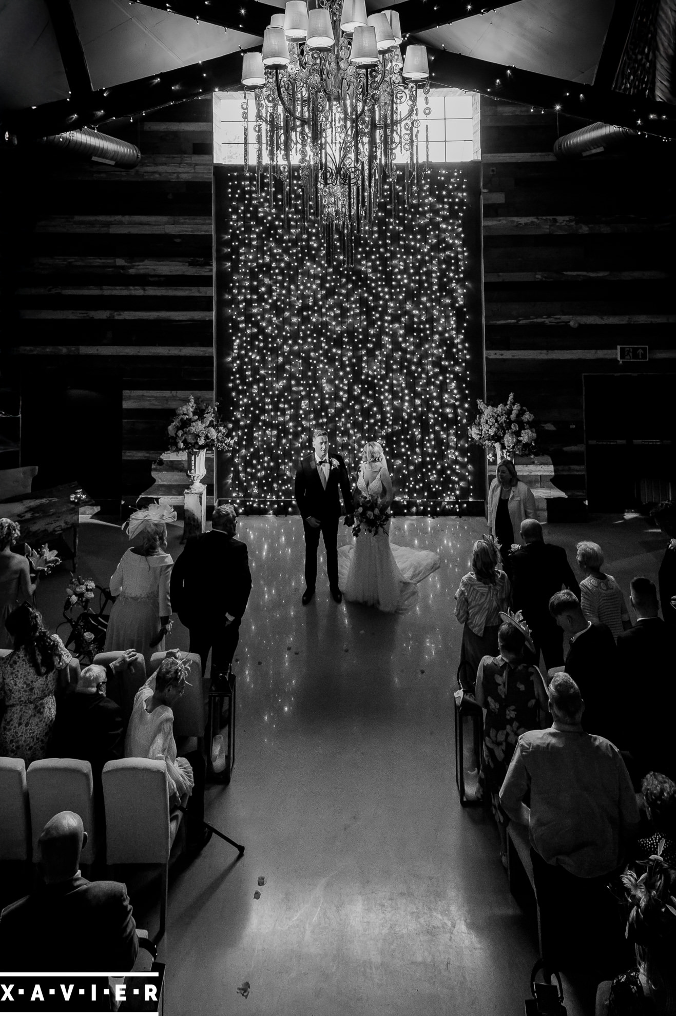 bride and groom stand by the glitter wall during the ceremony