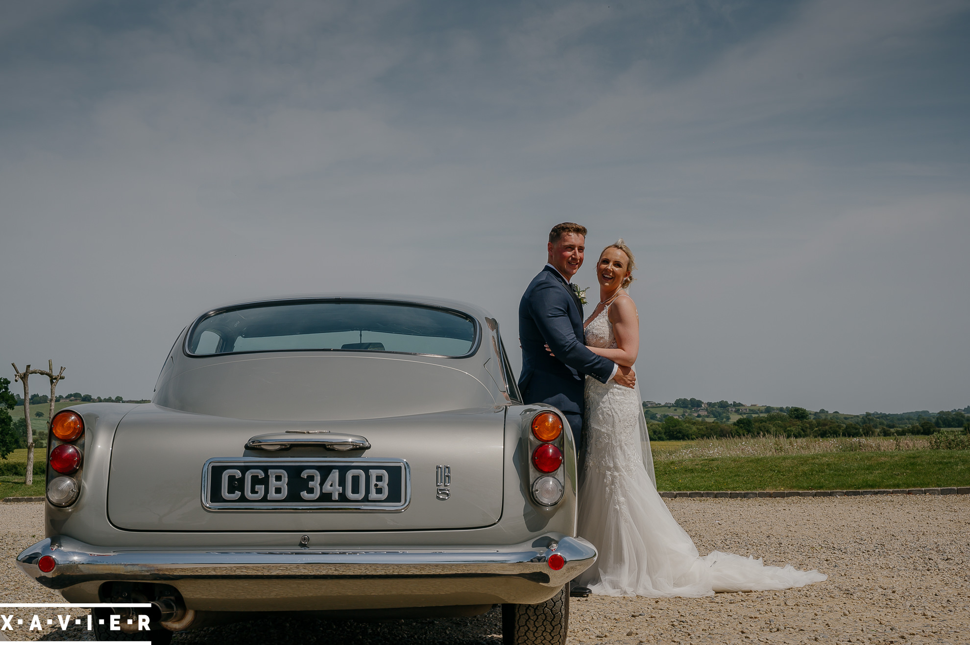 bride and groom satnd next to aston martin db5 wedding car