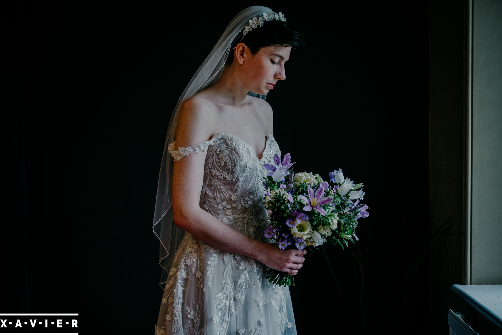 bride stands by the window holding her flowers